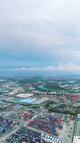 vertical aerial view of northport in klang, malaysia, revealing container terminals, port infrastructure, and a sprawling cityscape under a partly cloudy sky. uhd.