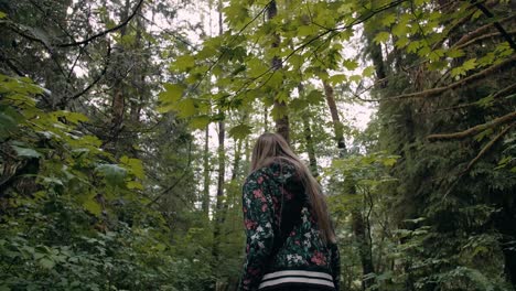 low angle shot following a blond woman walking on a moody forest in vancouver lynn valley