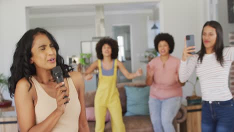 Happy-diverse-female-friends-singing-into-microphone-in-living-room