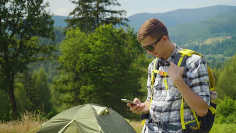 a young man with a backpack use a smartphone in the camping always in touch app for tourism