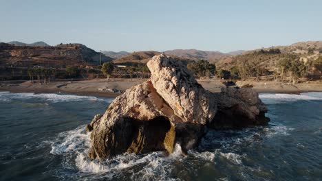 Aerial-view-of-crashing-waves-against-rock-at-sandy-beach-of-playa-Peñon-del-Cuervo-in-Malaga-at-summer