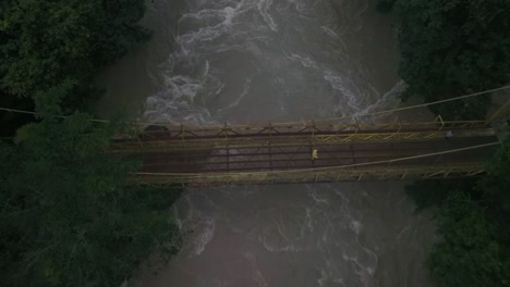 Man-walking-on-yellow-bridge-over-cahabon-river-at-Guatemalan-jungle,-aerial