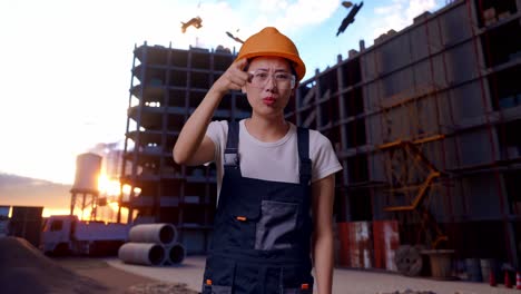 trabajadora asiática con gafas de protección y casco de seguridad gritando a la cámara mientras está de pie en el sitio de construcción
