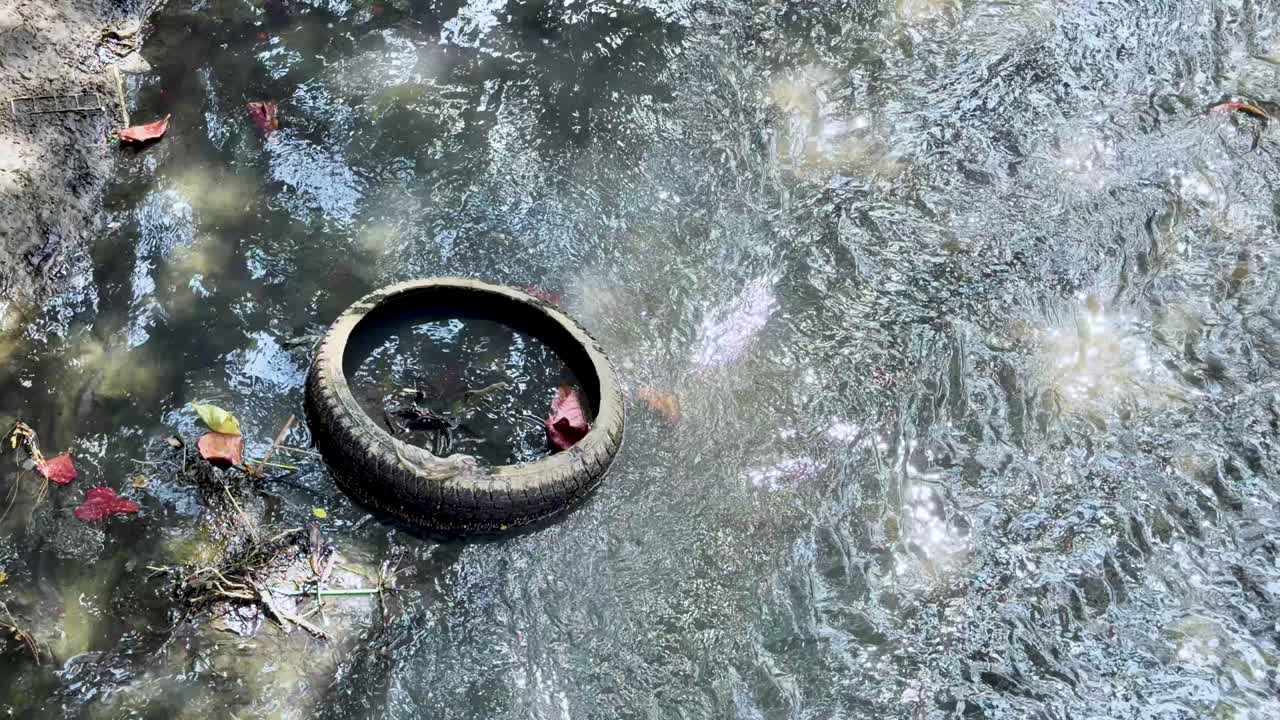 High angle shot of a rubber tire and garbage floating in murky flowing river water