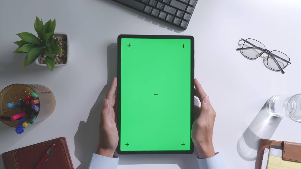 верхний вид ноутбука с макетным зеленым экраном chromakey на деревянном офисном столе рядом с ноутбуком с ручками, очками и стаканом воды.