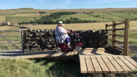 Women-on-mobility-scooter-navigating-ramps-and-gate-in-countryside-location