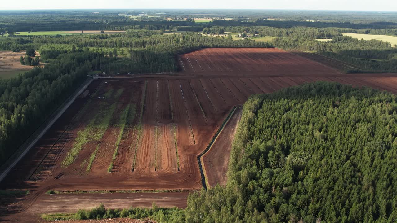 Aerial view of a large peat bog harvesting site with long parallel rows of extracted peat, wooden pallets, and covered stacks stretching across the landscape