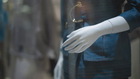 primer plano de un maniquí en un elegante traje de vaqueros con cinturón, la mano descansando en el lado, exhibido en la ventana de la tienda con fondo borroso y efectos de luz bokeh en el vidrio