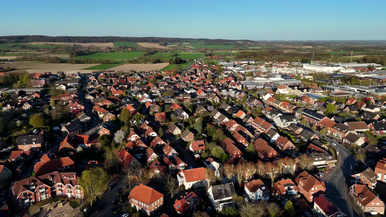 Historic small german town with orange tile roofs during golden sunset in spring. Slow drone flyover shot.Green and yellow countryside farm fields in distance. Wide shot.Single family house in village