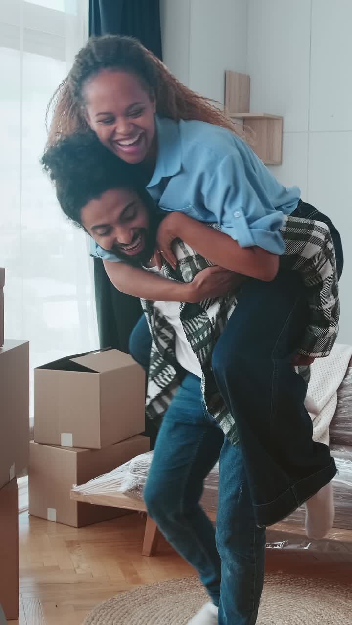Young man riding girlfriend on back and spinning in place in house after moving