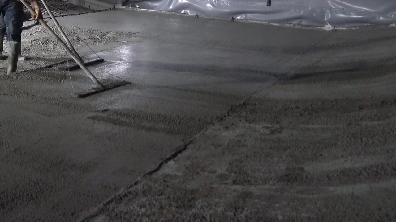 Construction workers in safety boots leveling fresh concrete over steel rebar grid during a night shift [cite: AA_17.jpg]. Detail shot of industrial slab pouring and site operations