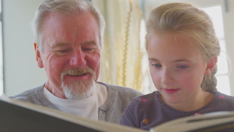 close up of grandfather and granddaughter looking through photo album in lounge at home together