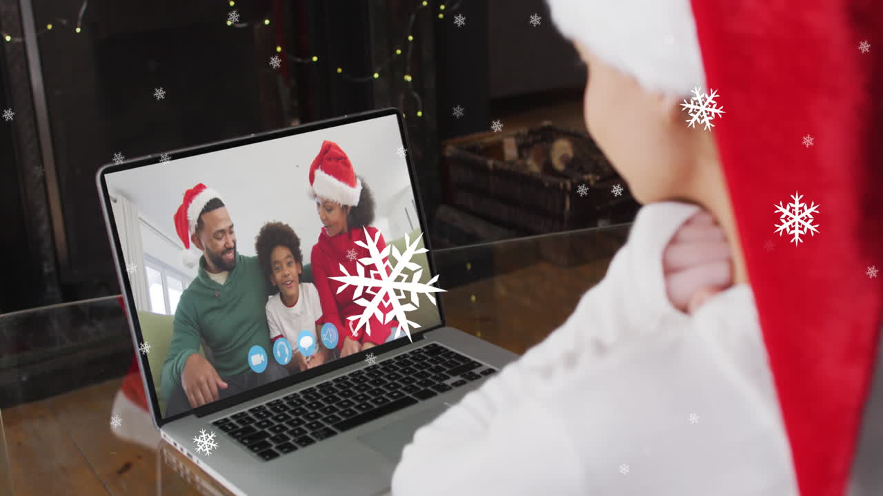 animación de nieve cayendo sobre una mujer sonriente en sombrero de santa en una llamada de video portátil con su familia