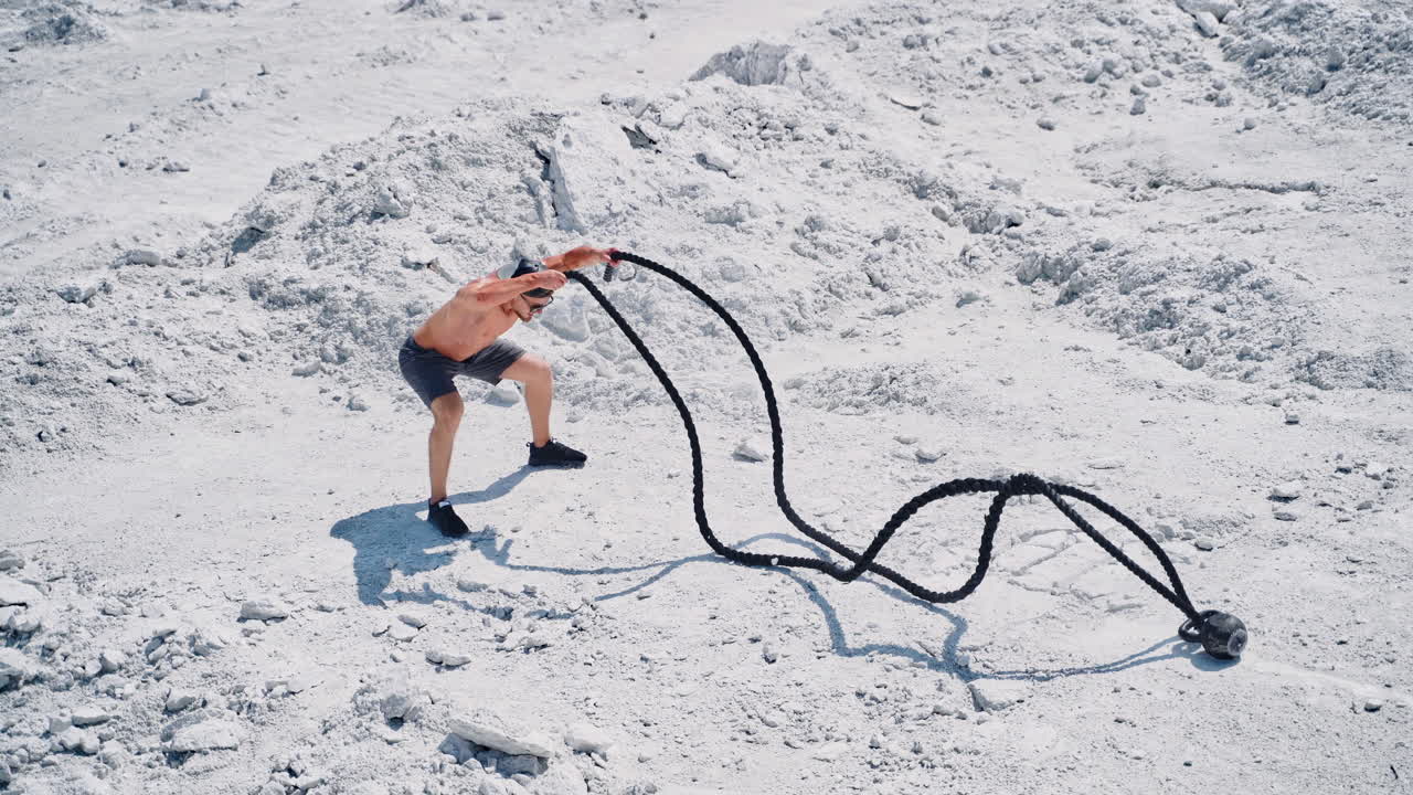 Aerial shot of a man working out with battle ropes. Bodybuilder posing outdoors.