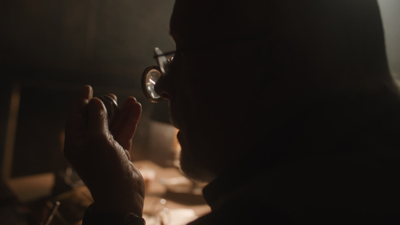 Older passionate man evaluates an old silver skull watch in his office at night