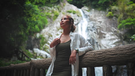 Woman-stands-in-front-of-majestic-waterfall,-enjoying-the-natural-beauty-and-peaceful-atmosphere