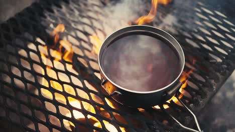 Boiling-hot-glogg-on-a-grill-over-campfire-in-woods-in-winter-in-Lemmenlaakso,-Finland