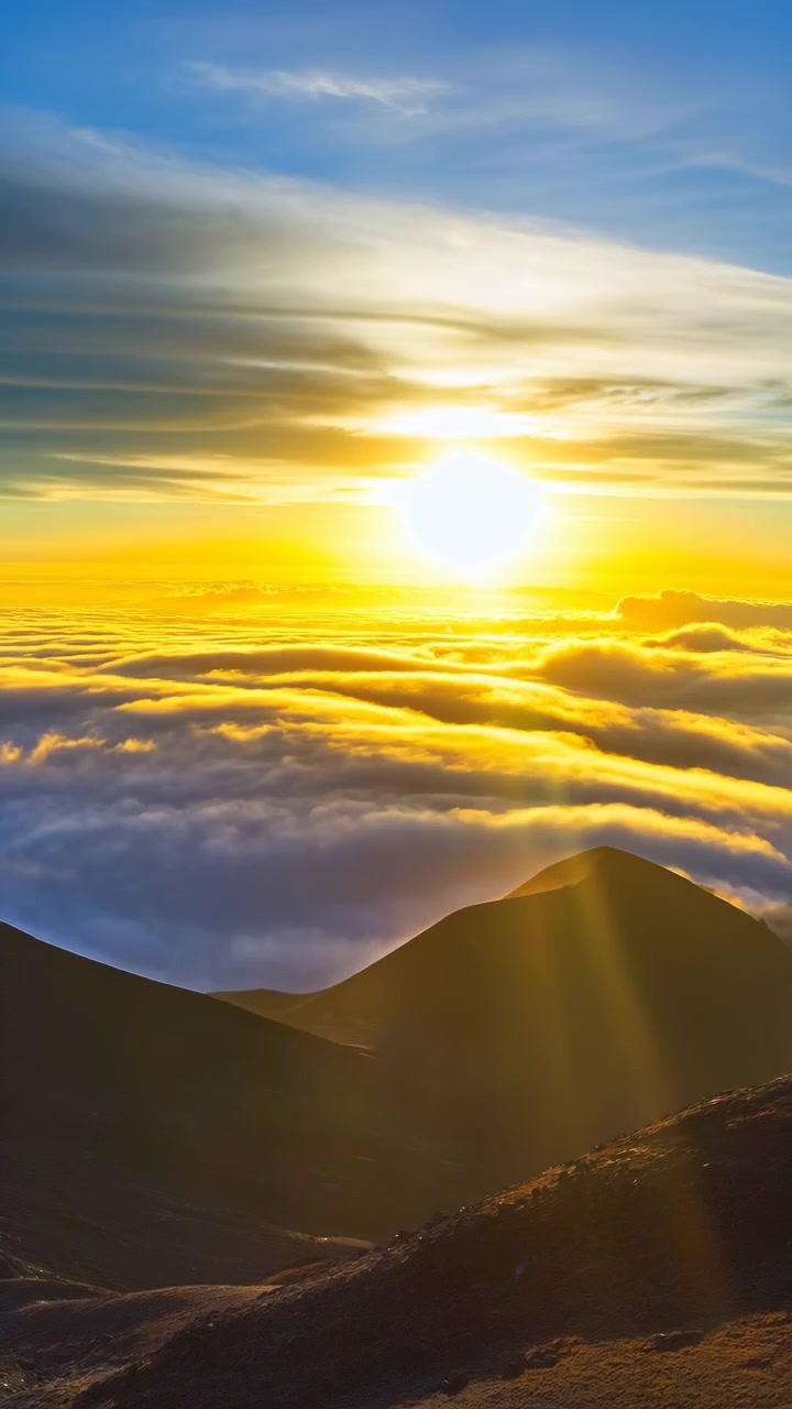 Alba su un mare di nuvole, cime montuose, calda luce dorata si riversa su una coperta di nuvole ondulate, scure e in silhouette