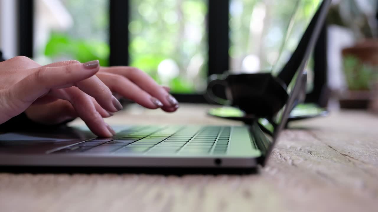 A woman's hands working and typing on laptop keyboard on wooden table