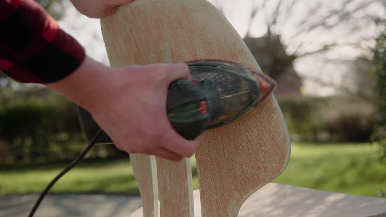 toma detallada de un manitas que usa una máquina pulidora para restaurar una silla de diseño antiguo en el jardín en un día soleado 4k