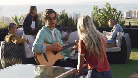 Young-man-playing-guitar-on-a-rooftop-with-his-friends