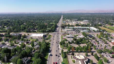 drone pushes in and tilts down over a steady flow of traffic. there are lots of visible trees, homes and businesses.