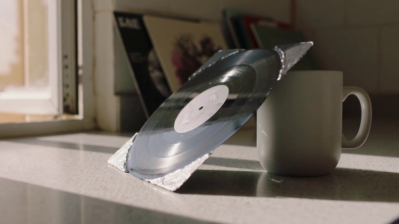 Roterende zwarte vinylplaat leunend tegen mok op aanrecht, zonlicht raakt foliewig