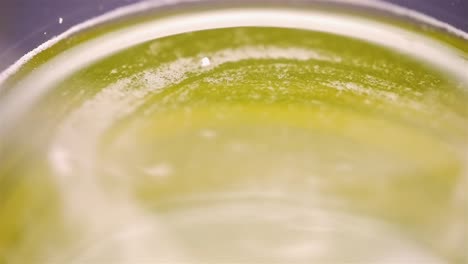 top down view of viscous yellow liquid spinning along curved rim edge of glass, slow motion