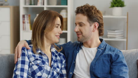 close up of the young attractive man and woman sitting close on the sofa and talking, then their small daughter running to them and hugging