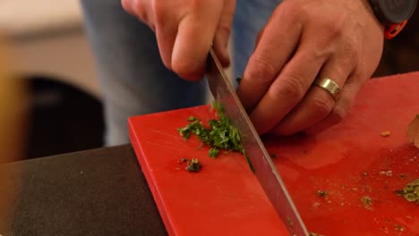person chopping herbs, greens with chef's knife while cooking.