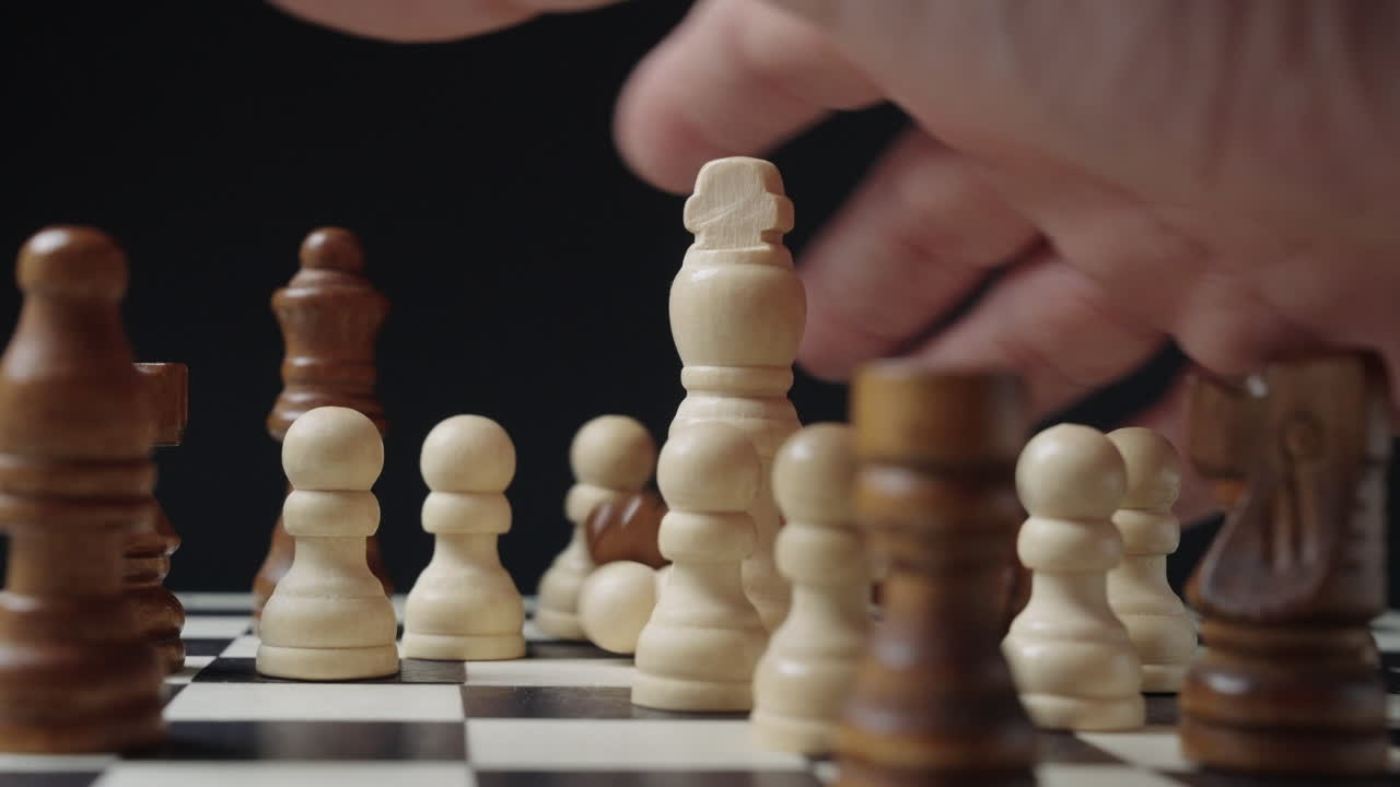 Mano che rovescia violentemente i pezzi degli scacchi sulla scacchiera. Concetto di fallimento, frustrazione, crisi, reazione emotiva, crollo della strategia o interruzione improvvisa.