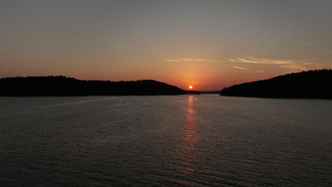 flyover of boat riding towards bright orange sunset on arkansas lake, aerial view