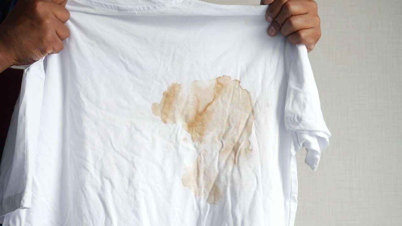 커피 얼룩이 있는  티셔츠를 들고 있는 남자.