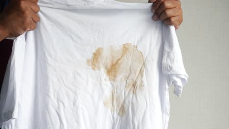 a man holding a white t-shirt with a coffee stain on it.