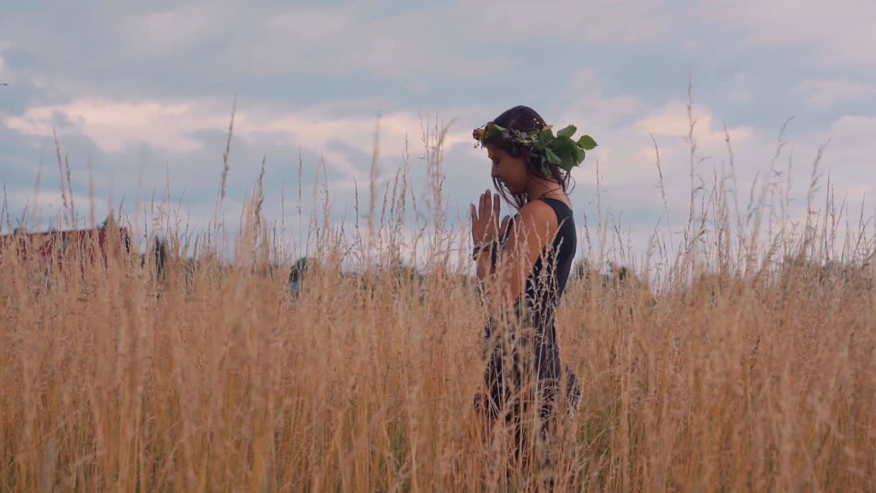Hipster girl stands between tall grass putting palms together to pray for world