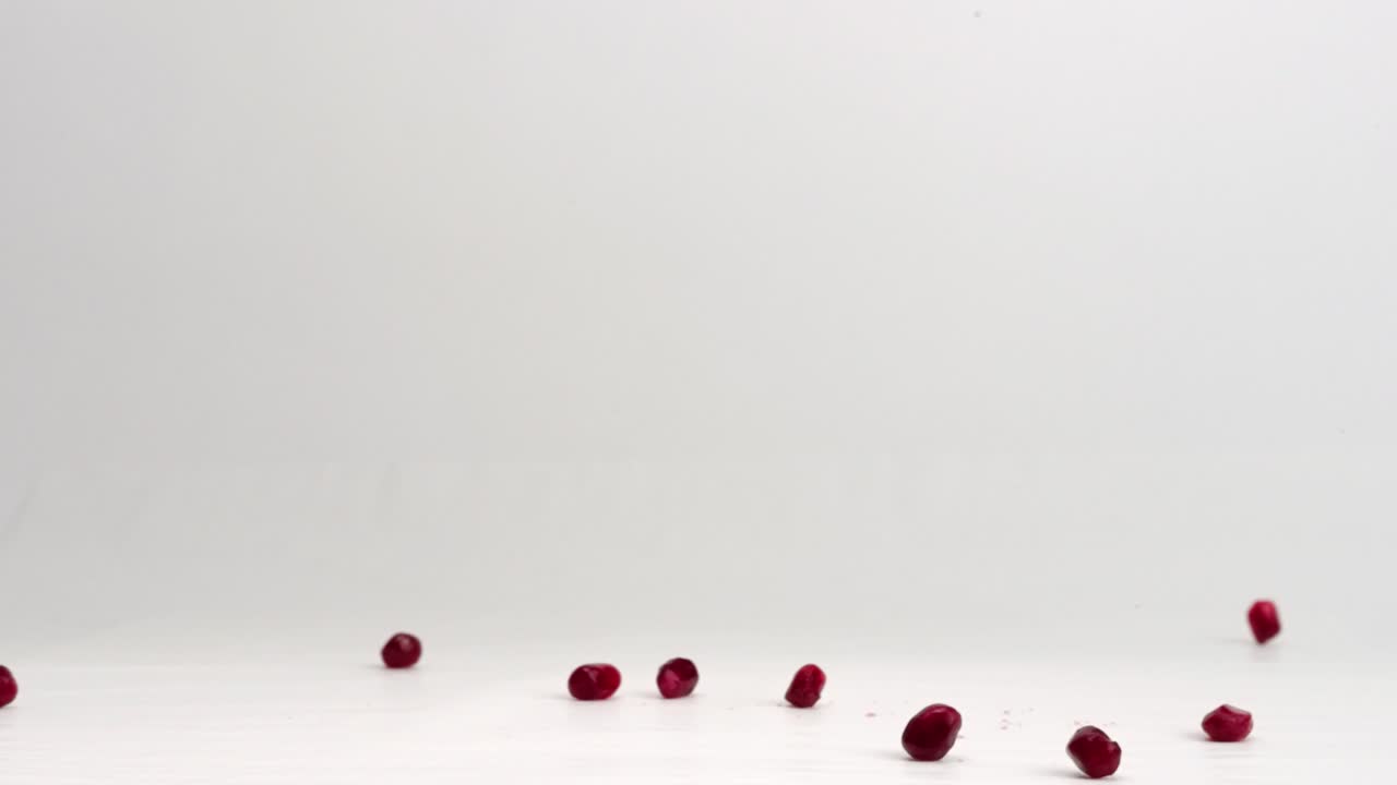 arilos de granada roja cayendo sobre el fondo del estudio blanco y rebotando en cámara lenta de 4k