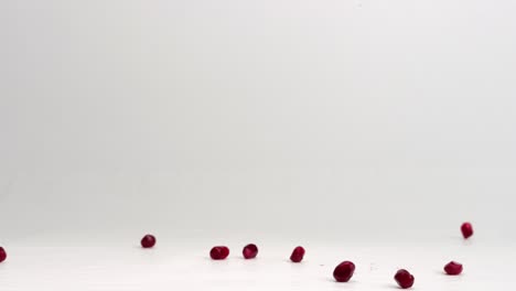 Red-pomegranate-arils-falling-onto-white-studio-backdrop-and-bouncing-in-4k-slow-motion