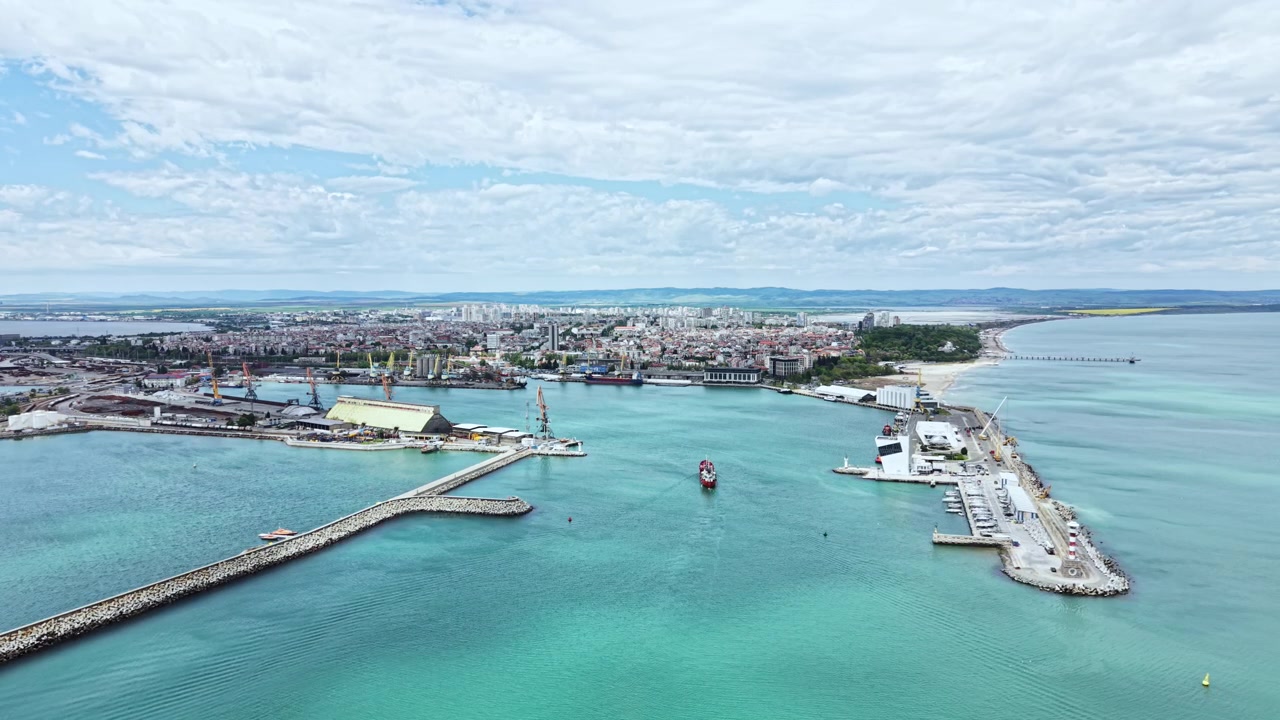 Vista di una città sul mare con strutture portuali e barche sotto un cielo nuvoloso, che mostra l'incontro tra terra e acqua durante il giorno