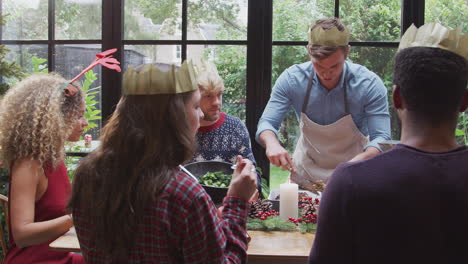 group of friends sitting around dining table at home as vegetarian christmas dinner is served