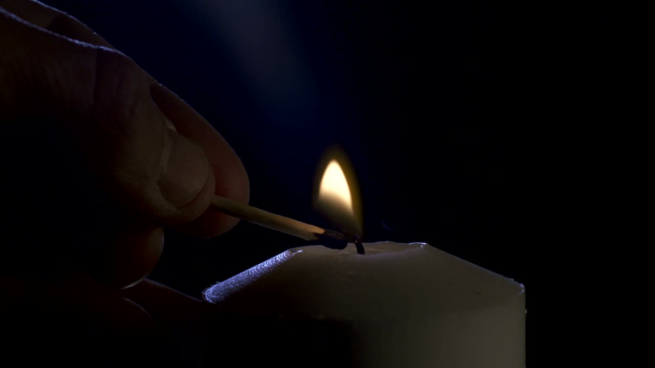 imágenes macro en cámara lenta de una vela blanca encendida por un fósforo sobre un fondo oscuro