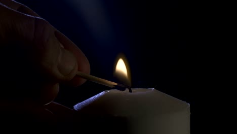 slow motion macro footage of a white candle lit by a match on a dark background