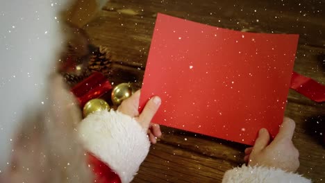 video composition with falling snow over desk with santa holding red card