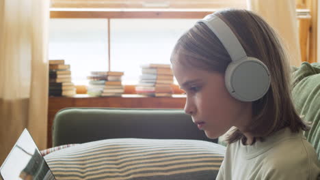 Close-Up-Of-A-Pretty-And-Intelligent-Blonde-Little-Girl-With-Headphones-Looking-At-The-Laptop-Screen