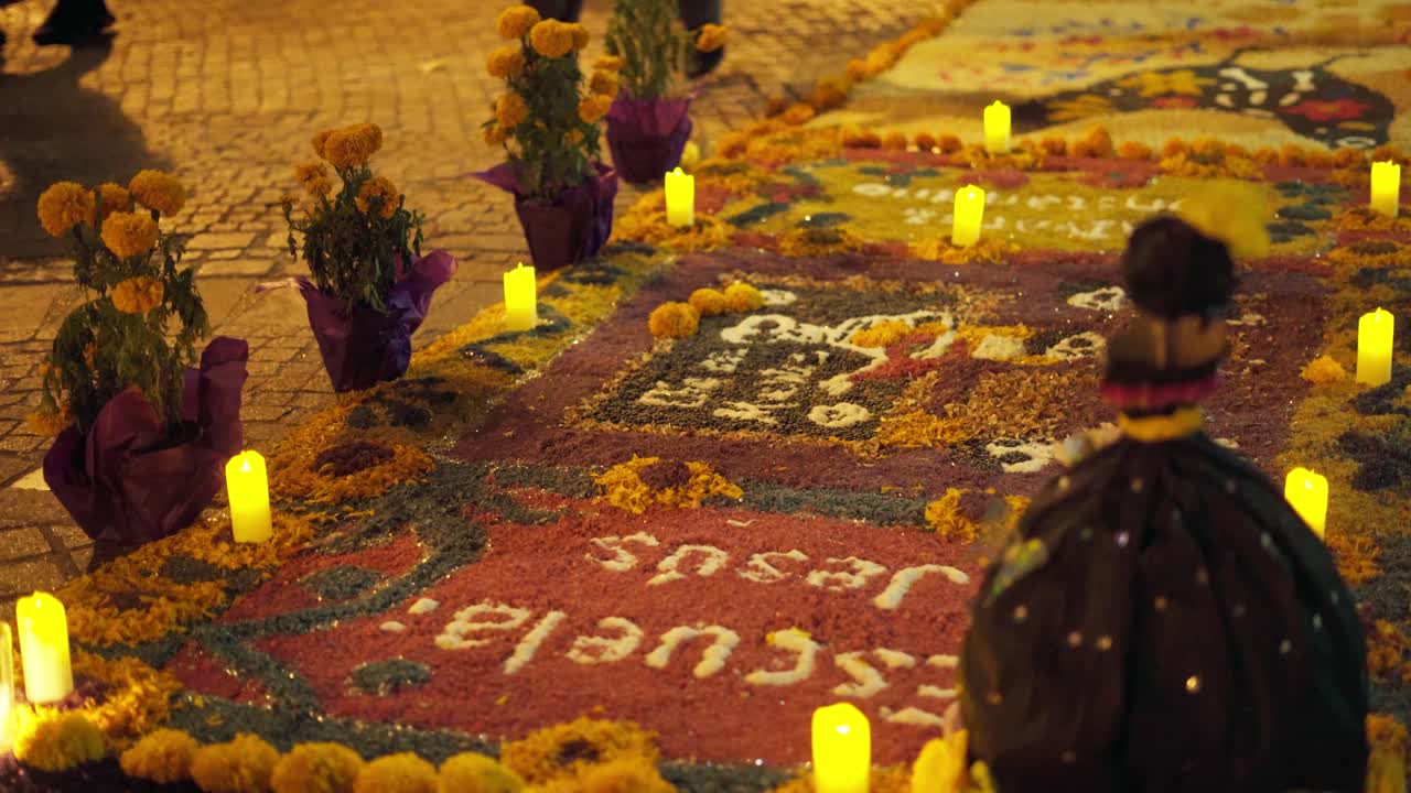 A nighttime walkway lined with glowing candles, marigold flowers and intricate street carpets crafted from colored materials forming cultural patterns and festive motifs during traditional celebration