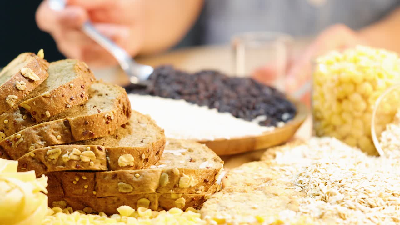 A close-up of whole grain bread, pasta, and grains being prepared in a well-lit kitchen setting
