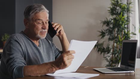 Shocked-caucasian-senior-man-looking-at-laptop-and-having-phone-call.