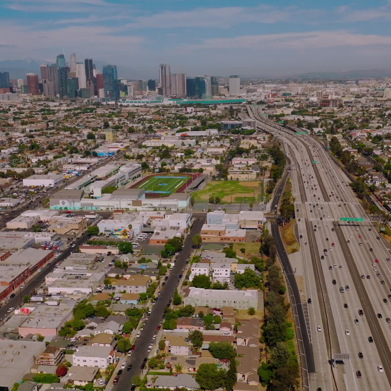 Multiple cars moving to and from financial downtown Los Angeles, California. Enormous urban territory of low buildings on sunny day