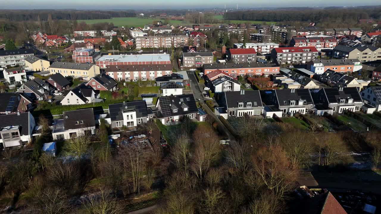 New Housing area in small town with solar panels on roof in winter season. Leafless trees during sunrise. Aerial lateral wide shot. Apartment blocks in background.
