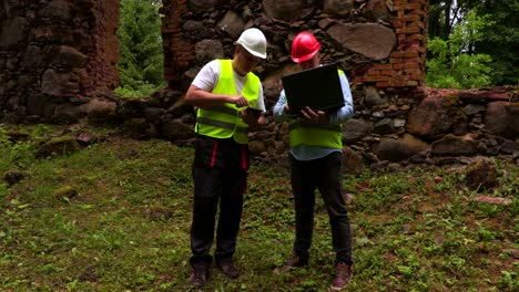 engineers with laptop and tablet pc near old wall ruins