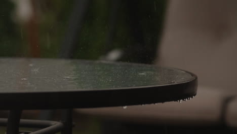 Heavy-rain-falling-onto-and-dripping-off-of-glass-table,-Slow-Motion